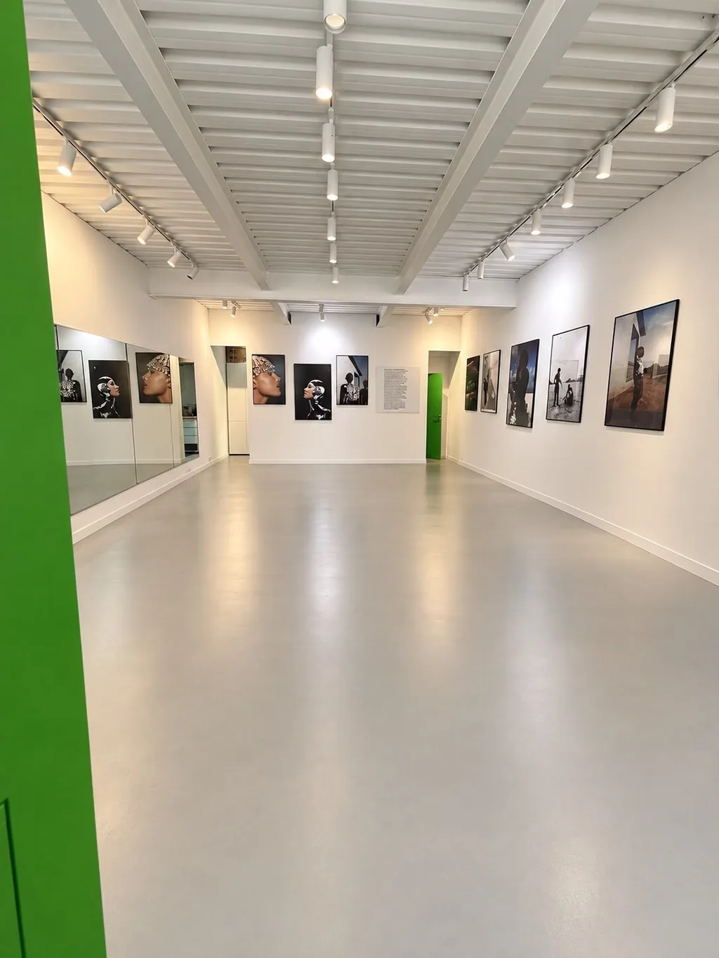 Galerie NEXT : longue salle lumineuse aux colonnes vertes, photographies encadrées sur les murs et plafond blanc à poutres apparentes
